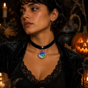 May include: A black velvet choker necklace featuring a round silver-toned pendant with a colorful, iridescent gradient background and a dark, stylized DNA-like helix symbol centered on the surface, worn around the neck with a black lace-trimmed top.