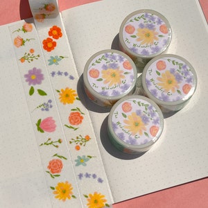 May include: Four rolls of washi tape with floral designs and the text "The Wednesday Co." on each roll. The tape is on a white background with small dots.