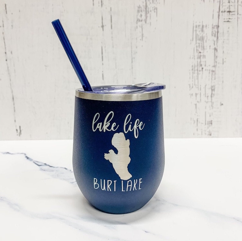 May include: A navy blue stainless steel tumbler with a white lid and a blue straw. The tumbler has the text "lake life" and "Burt Lake" printed on it in white.