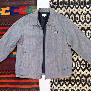 May include: A gray and white striped jacket with a zipper closure and a small patch on the left chest that says "Prank".