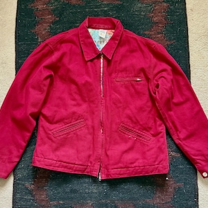 May include: A bright red jacket with a collared neckline, a zipper closure, and two front pockets. The jacket has a patterned lining visible at the collar and a small pocket on the chest. The jacket is a solid color and has long sleeves.