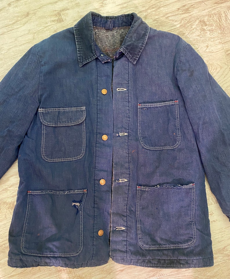 May include: A dark blue denim work jacket with multiple pockets and brass buttons. The jacket has a corduroy collar and a lined interior.
