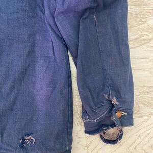 May include: A dark blue denim jacket with a frayed hem and a small hole on the left side. The jacket has a button closure and a single button on the right sleeve.