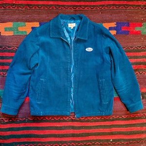 May include: A teal blue corduroy jacket with a zipper closure and a small, white oval patch with the word "Panda" on it.