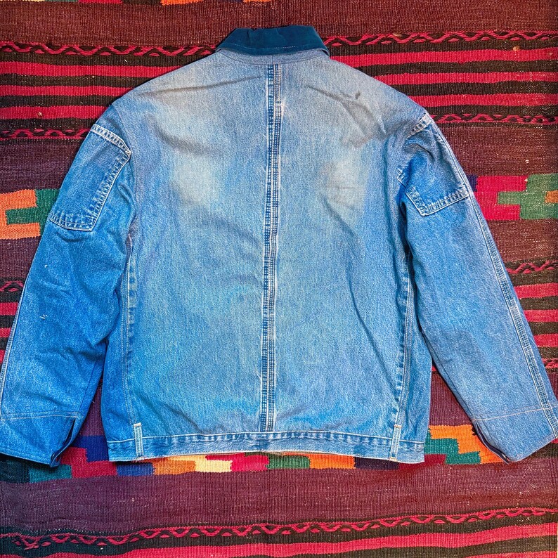 K&ouml;nnte beinhalten: Eine blaue Jeansjacke mit dunkelblauem Kragen und einem einzigen Knopfverschluss. Die Jacke hat einen leicht verblassten Look und ist aus einem weichen, bequemen Material gefertigt.