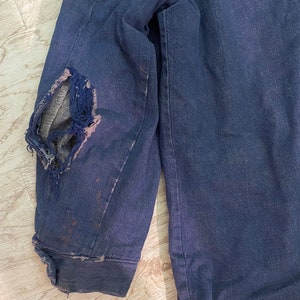 May include: A dark blue denim jacket with a large hole in the elbow. The jacket is worn and has a faded appearance.