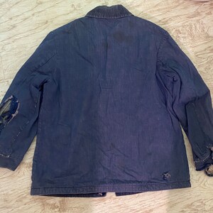 May include: A dark blue denim jacket with a button-up front and long sleeves. The jacket has a few small tears and a patch on the left sleeve.