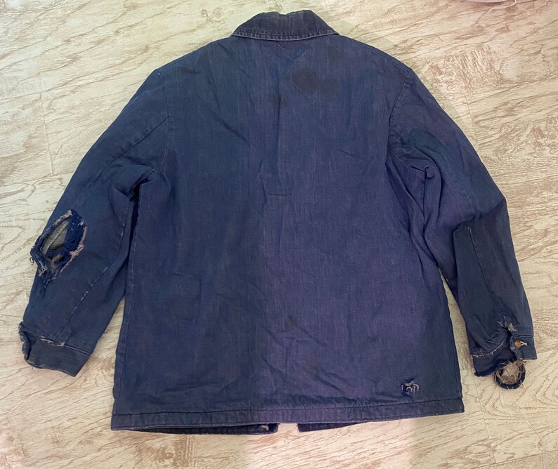 May include: A dark blue denim jacket with a button-up front and long sleeves. The jacket has a few small tears and a patch on the left sleeve.