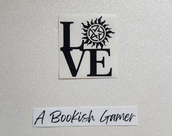May include: Black and white vinyl sticker with the word "LOVE" with a stylized sun and pentagram symbol in the "O". The sticker is on a white background. The text "A Bookish Gamer" is written in black on a white background below the sticker.