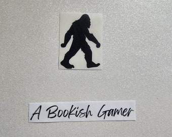 May include: Black silhouette of Bigfoot walking to the right on a white background. The text "A Bookish Gamer" is written on a white rectangle below the silhouette.
