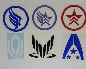 May include: A collection of six stickers featuring various geometric designs and symbols in blue, purple, red, and black. The stickers are on a white background. The designs include stars, wings, and abstract shapes.