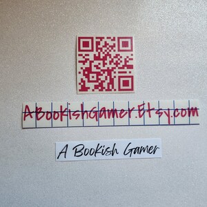 May include: A red and white QR code with the text "A Bookish Gamer.Etsy.com" and "A Bookish Gamer" written in red ink on white paper.