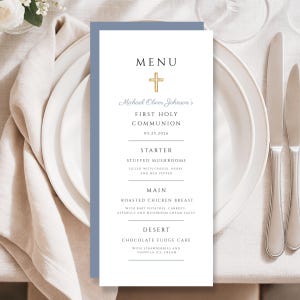 May include: A First Holy Communion menu card with a gold cross and the text "Menu". The menu includes starter, main, and dessert options. The card is white with a blue border and is set on a white plate with silverware.