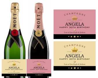May include: Two champagne bottles with personalized labels. The labels are pink and cream with gold accents. The text on the labels reads "Champagne", "Epernay France Fonde en 1743", "Angela", "Happy 30th Birthday", "Lots of love Kayla & Jackson".