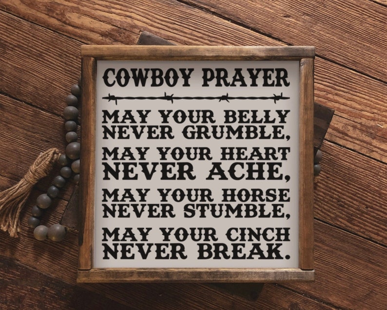 Peut inclure: Panneau en bois encadr&eacute; avec l'inscription "COWBOY PRAYER" et un po&egrave;me. Le fond est blanc avec du texte noir et un motif de fil de fer barbel&eacute;. Le cadre est de couleur marron fonc&eacute;, pos&eacute; sur une surface en bois.