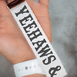 May include: White canvas keychain with black text that reads "& Yeehaws".