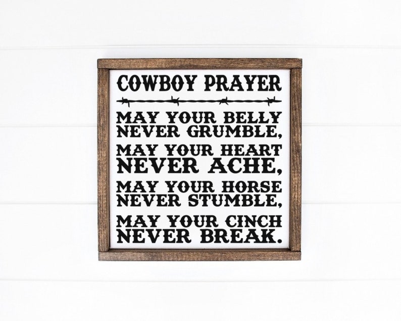 Peut inclure: Un panneau en bois encadr&eacute; avec le texte "COWBOY PRAYER" en noir, accompagn&eacute; d'un motif de fil de fer barbel&eacute;. La pri&egrave;re se poursuit avec les phrases "MAY YOUR BELLY NEVER GRUMBLE", "MAY YOUR HEART NEVER ACHE", "MAY YOUR HORSE NEVER STUMBLE" et "MAY YOUR CINCH NEVER BREAK."