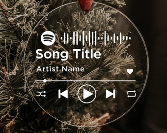 May include: A clear round ornament with a Spotify logo, a barcode, the text "Song Title" and "Artist Name", and a play button. The ornament is hanging on a Christmas tree.