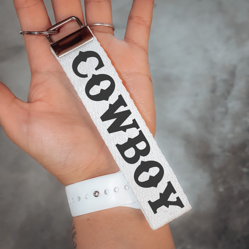 May include: White canvas keychain with a black "COWBOY" text in a vintage font.