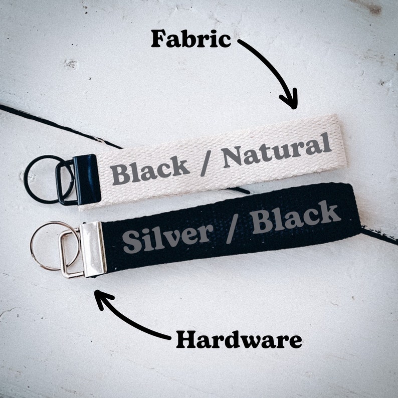 May include: Two keychains with black and silver hardware. The top keychain is made of natural fabric with black text that reads "Black / Natural". The bottom keychain is made of black fabric with silver text that reads "Silver / Black".