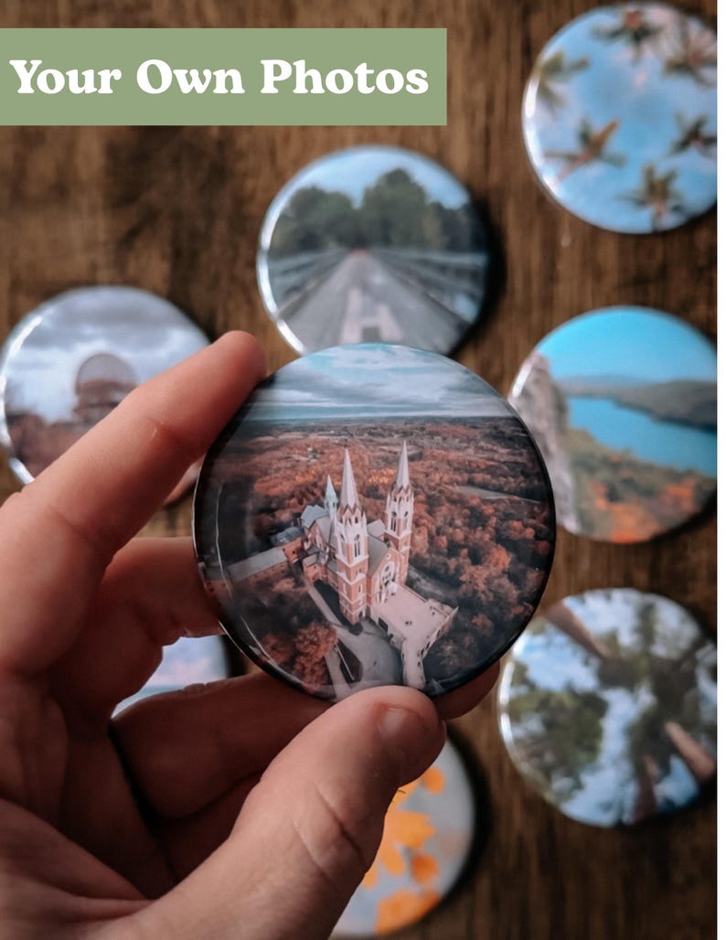 Pu&ograve; includere: Una collezione di bottoni rotondi e colorati con varie immagini stampate su di essi. I bottoni presentano immagini di una chiesa, una strada, un lago e alberi. Il testo "Your Own Photos" &egrave; stampato su uno sfondo verde nella parte superiore dell'immagine.