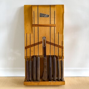 May include: A wooden knife block with a set of knives and a carving fork. The block is light brown and has the word "Ronaglo" printed on it.
