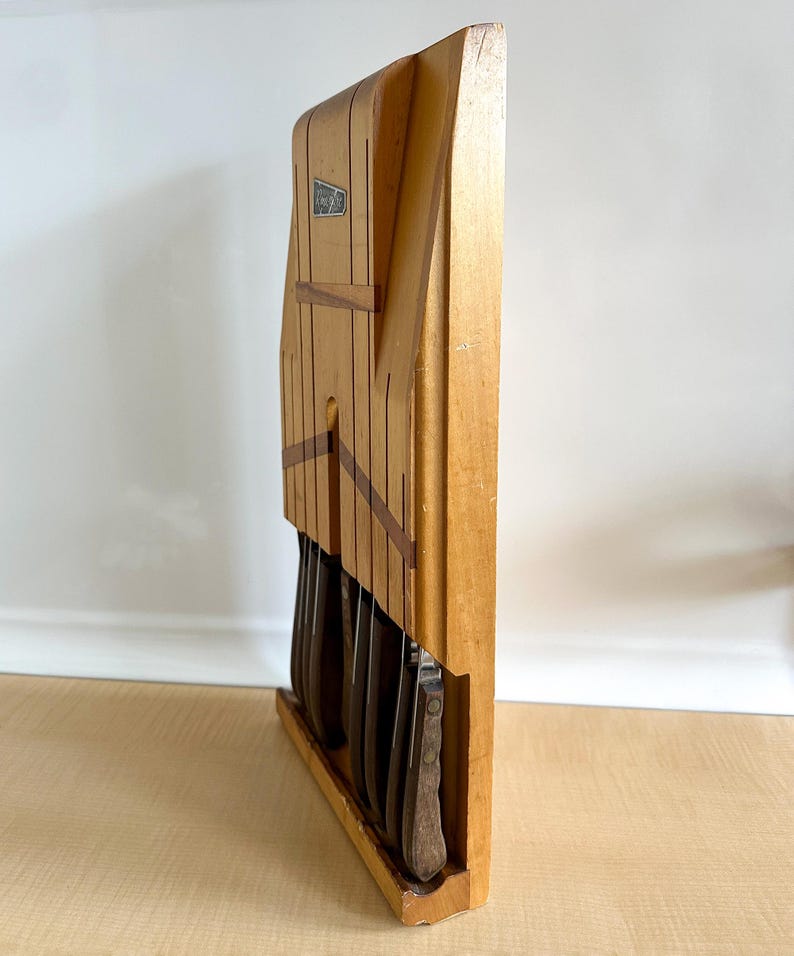May include: Wooden knife block with a set of knives. The block is made of light wood with dark wood accents. The knives are all metal with brown handles.