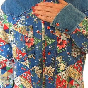 May include: A blue denim shirt with a patchwork design featuring floral patterns in red, yellow, and green. The shirt has a pointed collar and a button-up front.