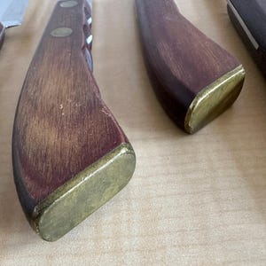 May include: Close-up of a wooden knife handle with a brass cap. The handle is dark brown with a reddish hue and has a smooth, polished finish.