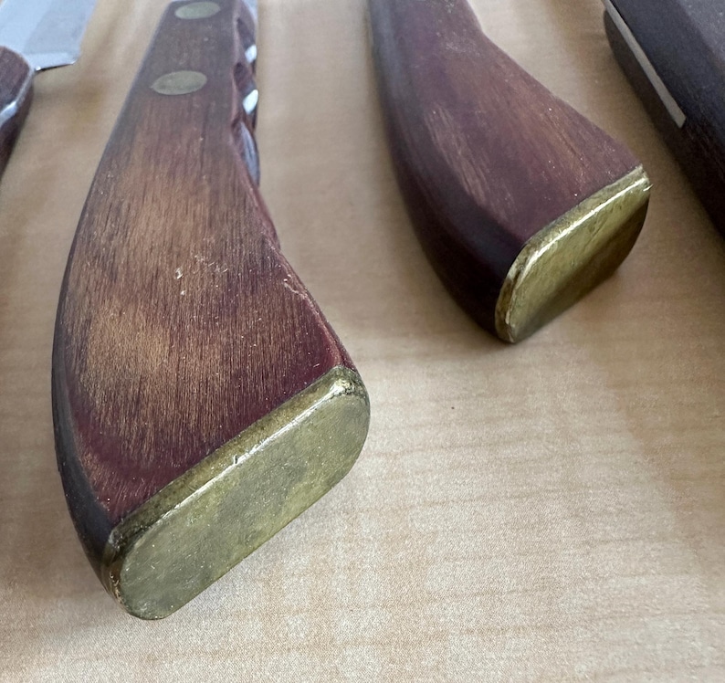 May include: Close-up of a wooden knife handle with a brass cap. The handle is dark brown with a reddish hue and has a smooth, polished finish.