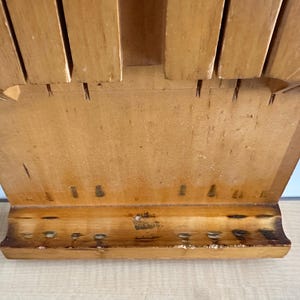 May include: A wooden knife block with slots for holding knives. The block is made of light brown wood and has a rectangular shape. The block has a small shelf at the bottom.