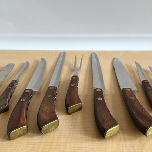 May include: Set of eight kitchen knives with wooden handles. The knives have stainless steel blades and brass accents. The knives are arranged on a wooden cutting board.