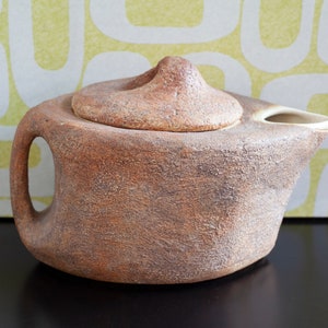 May include: A brown ceramic teapot with a textured surface and a lid. The teapot has a spout and a handle.