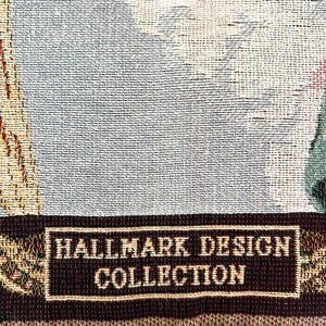 May include: A brown and cream woven tapestry throw blanket with a fringe border. The blanket features a woven label that reads "Hallmark Design Collection".