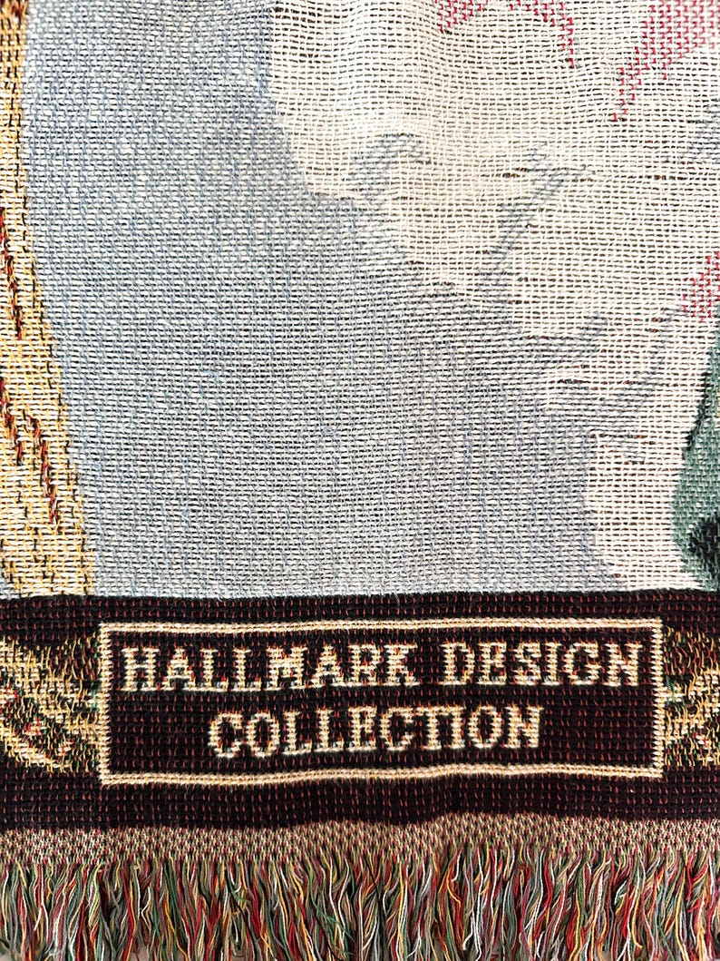 May include: A brown and cream woven tapestry throw blanket with a fringe border. The blanket features a woven label that reads "Hallmark Design Collection".