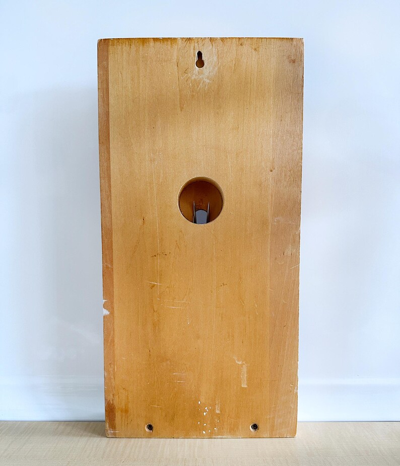 May include: A light wood wall mounted shelf with a circular hole in the center. The shelf has a small hole at the top for hanging.