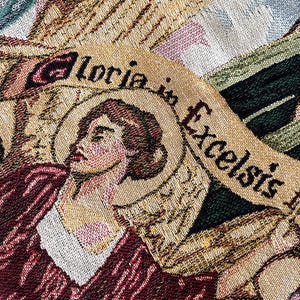 May include: A tapestry with a woman's face and the words "Gloria in Excelsis" woven into the fabric. The tapestry is made of a variety of colors, including gold, red, and green.
