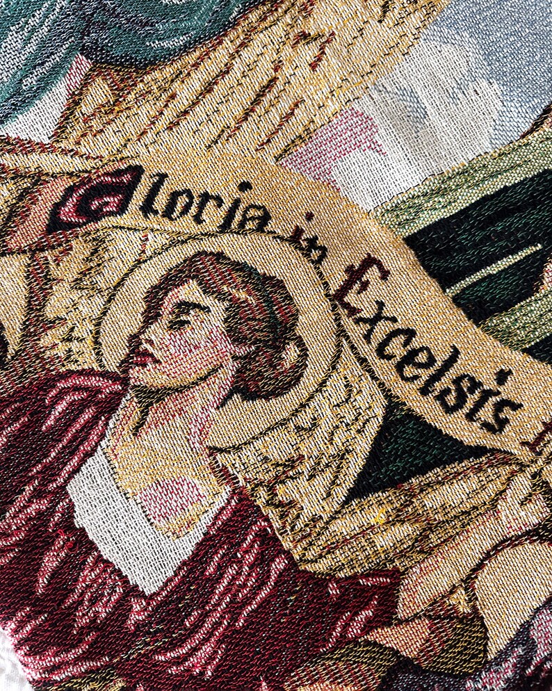 May include: A tapestry with a woman's face and the words "Gloria in Excelsis" woven into the fabric. The tapestry is made of a variety of colors, including gold, red, and green.