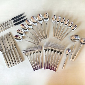 May include: A comprehensive stainless steel flatware set featuring multiple knives, forks, and spoons. The collection includes dinner knives, dinner forks, salad forks, soup spoons, teaspoons, and two large serving ladles, all with a polished finish.