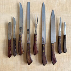 May include: Set of nine kitchen knives with wooden handles. The knives include a paring knife, a chef's knife, a bread knife, a utility knife, a boning knife, a carving knife, and a fork.