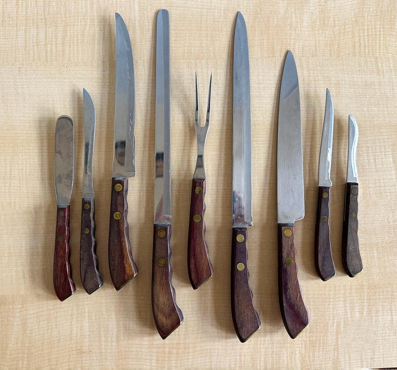 May include: Set of nine kitchen knives with wooden handles. The knives include a paring knife, a chef's knife, a bread knife, a utility knife, a boning knife, a carving knife, and a fork.