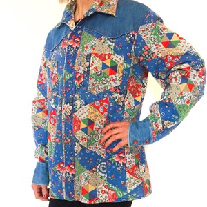 May include: A blue denim shirt with a patchwork design featuring various floral patterns in red, yellow, green, and white. The shirt has a pointed collar and a button-up front.