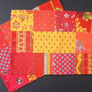 May include: Two rectangular placemats with a patchwork design. The fabric features a variety of patterns in red, yellow, and orange, including floral, paisley, and geometric motifs. The placemats are arranged on a dark surface.