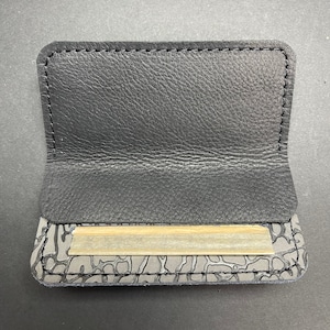 May include: A black leather rolling tray with a gray patterned design. The tray has a flap that opens to reveal a slot for rolling papers.