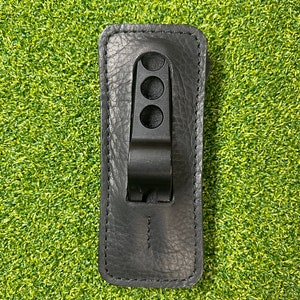 May include: Black leather holster with a metal clip and four holes. The holster is designed to hold a small object, such as a knife or a tool.