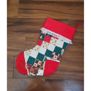 May include: A Christmas stocking featuring a patchwork design of red, green, and cream fabric squares with gingerbread men, hearts, and floral patterns. The stocking has a red cuff with white lace trim and a red toe and heel section.