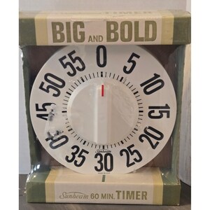 May include: A white Sunbeam 60-minute timer with a black dial and red indicator. The timer has the words "BIG AND BOLD" printed on the top and "Sunbeam 60 MIN. TIMER" on the bottom. The timer is in its original packaging.