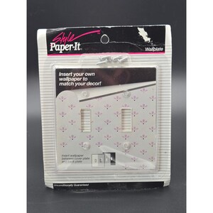 May include: A Style Paper-It brand double light switch wallplate in original packaging. The clear plastic cover allows for custom wallpaper insertion. The package includes mounting screws and features a white background with a pink floral pattern.