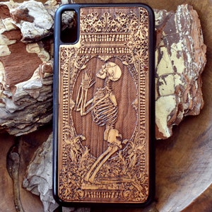 May include: A wooden phone case with an intricate design featuring a skeleton praying in a carved frame. The case is made of dark wood with a brown stain.