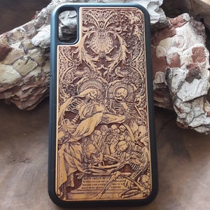 May include: A black phone case with a detailed wood-carved design. The design features skeletons and ornate patterns, with text at the bottom. The case has a black border and a light brown wood-grain centre.